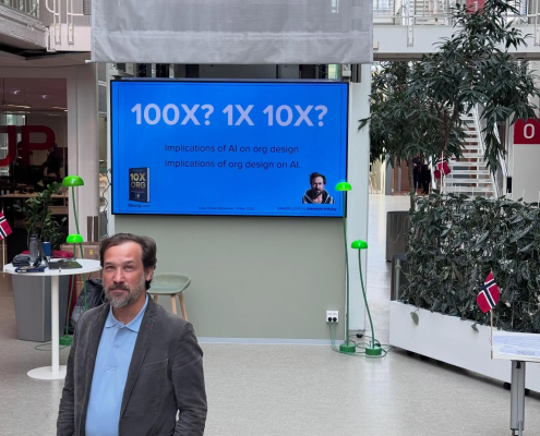 Alexey Krivitsky foran en stand og et banner for boken 10x Org og seminaret Redesign, then AI i Oslo Forskningspark.